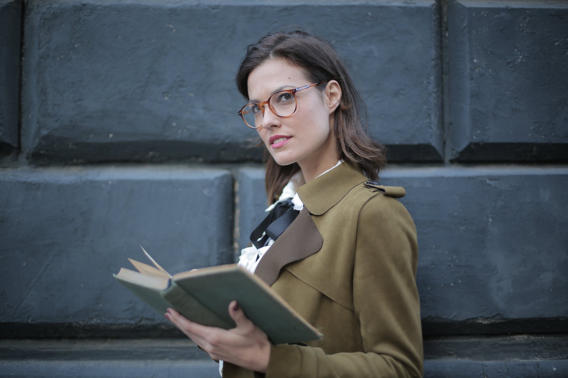 serious adult woman with open book on street against facade of old building in university